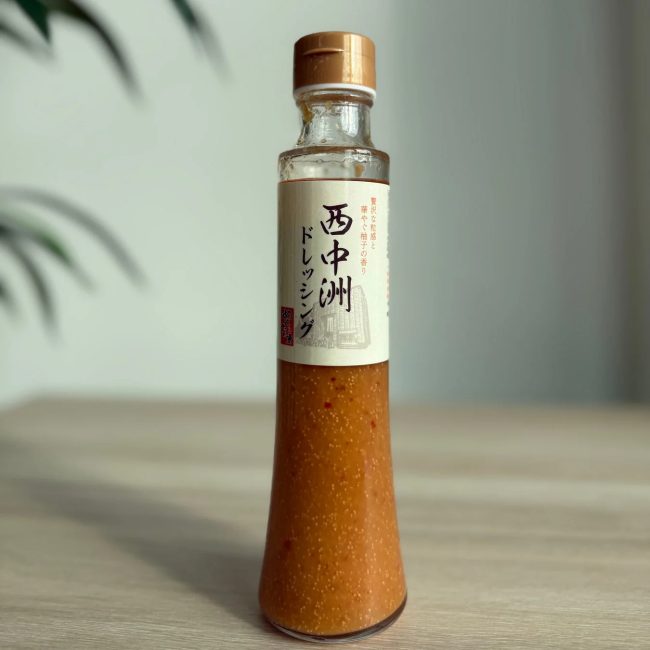 木製のテーブルに置かれた「西中洲ドレッシング」の瓶。贅沢な粒感と華やかな柚子の香りが特徴で、和食にも合う調味料です。