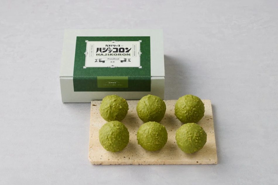 抹茶味の丸いお菓子「ハジコロソ」が6個、シンプルな石板の上に並べられ、その奥に同商品のパッケージ箱が置かれている。ギフトや手土産にぴったりの、上品で美味しそうなスイーツの様子。